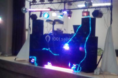 Installation de matériel de sonorisation et d'éclairage coloré sur une scène intérieure, avec des enfants au premier plan.