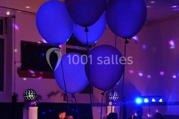 Des ballons bleus flottent dans une salle faiblement éclairée avec des lumières colorées et des projecteurs.