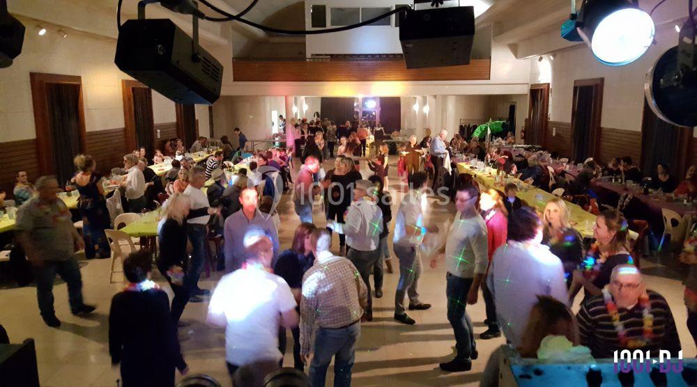 Salle animée avec des personnes dansant et discutant autour de tables, éclairée par des lumières colorées.