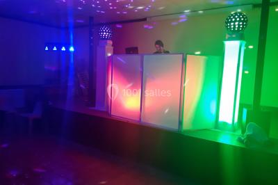 Un DJ mixant de la musique sur une table de mixage éclairée par des lumières colorées dans une ambiance nocturne.