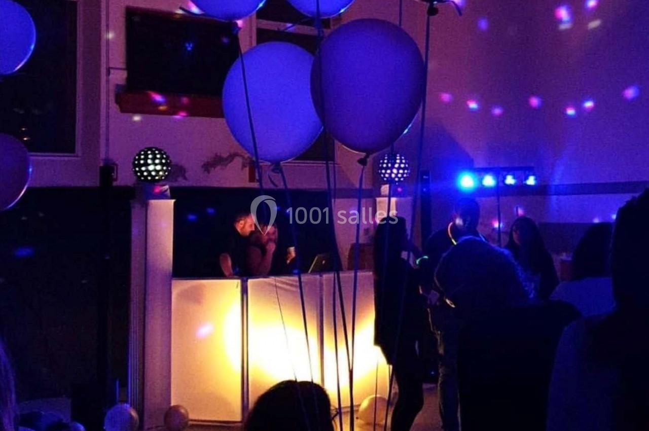 Des personnes dansent dans une salle faiblement éclairée avec un DJ en arrière-plan et des ballons suspendus.