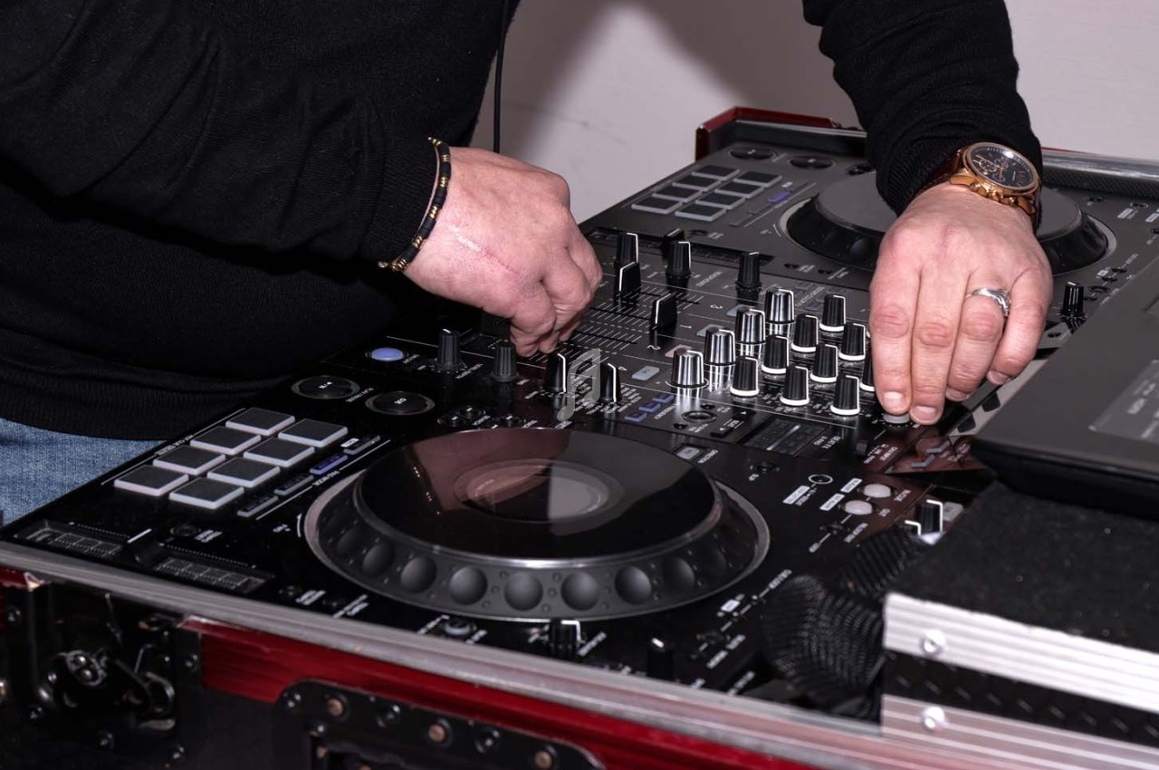 Un DJ ajuste les commandes d'une table de mixage avec des platines et divers boutons.