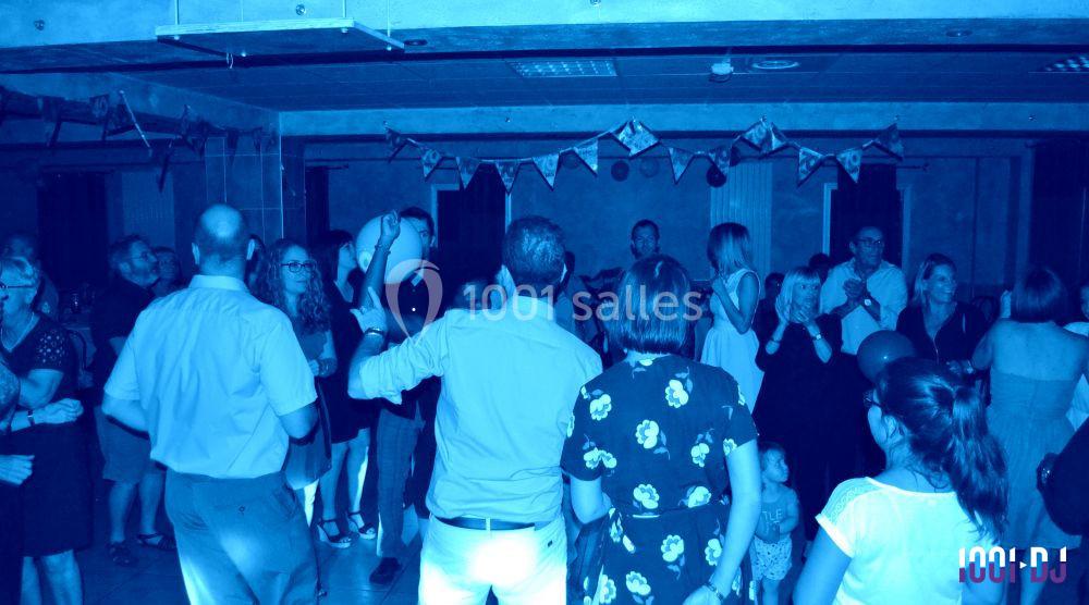 Des personnes dansent et discutent dans une salle décorée, éclairée par une lumière bleue tamisée.