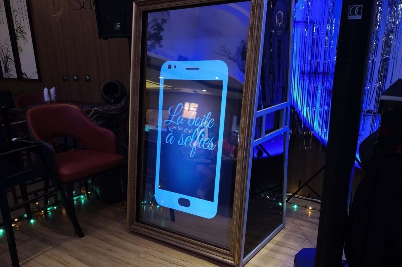 Miroir interactif en forme de smartphone avec l'inscription ’La boîte à selfies’, installé dans un espace décoré.