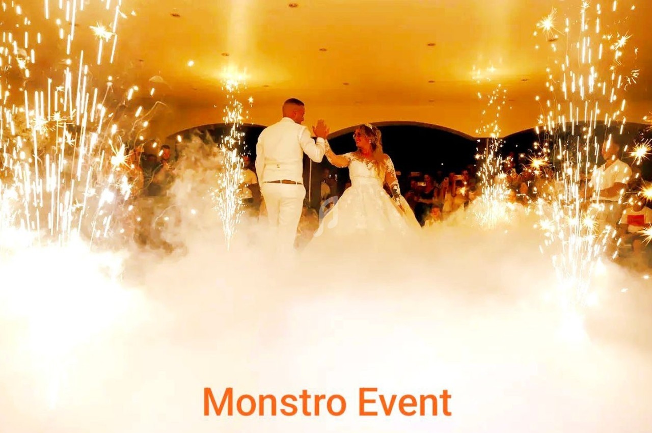 Un couple danse au centre d'une salle entourée d'effets pyrotechniques et de fumée blanche.