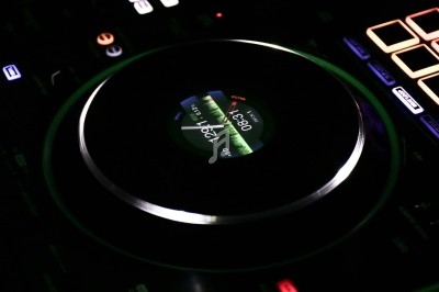 Une personne filme un DJ en train de mixer dans une salle éclairée par des lumières de scène.