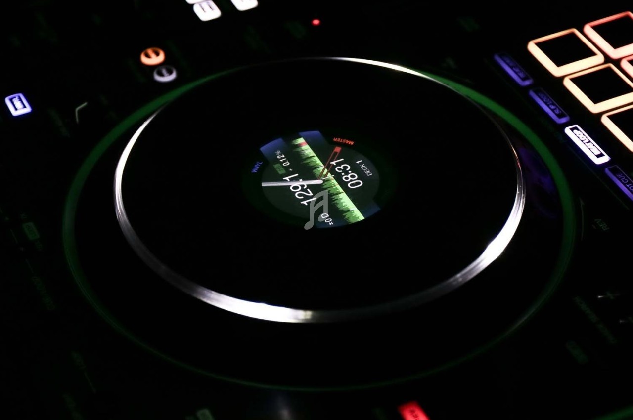 Platine de DJ avec écran central affichant une onde sonore lumineuse, entourée de commandes rétroéclairées.