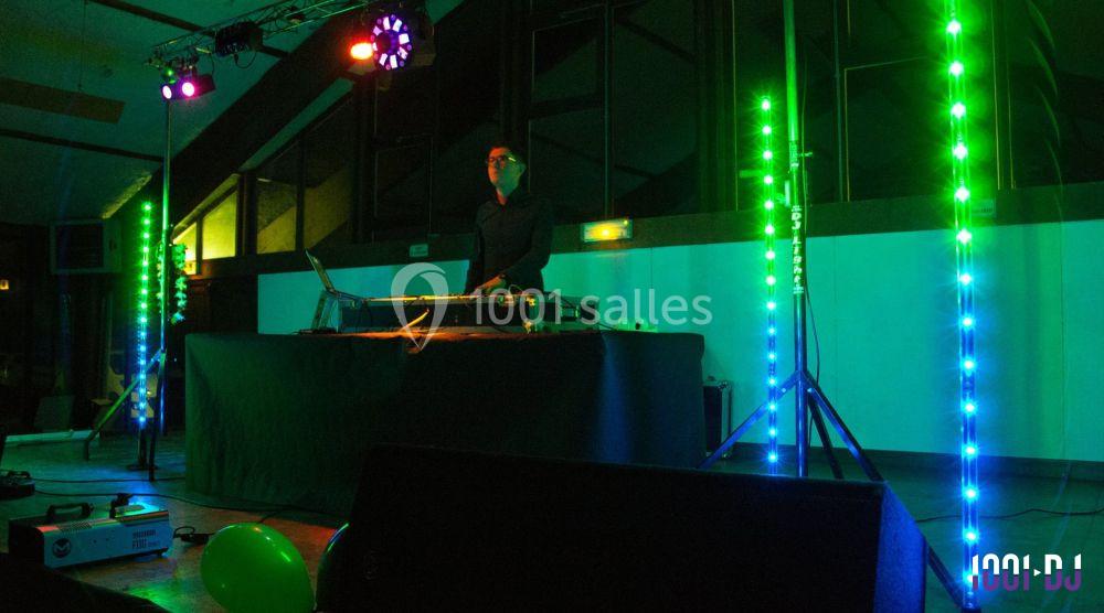 Un DJ mixe sur une scène éclairée par des lumières colorées dans une salle sombre.