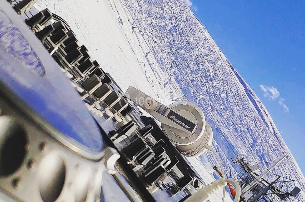 Platines DJ et casque audio posés en extérieur sur fond de montagne enneigée sous un ciel bleu.