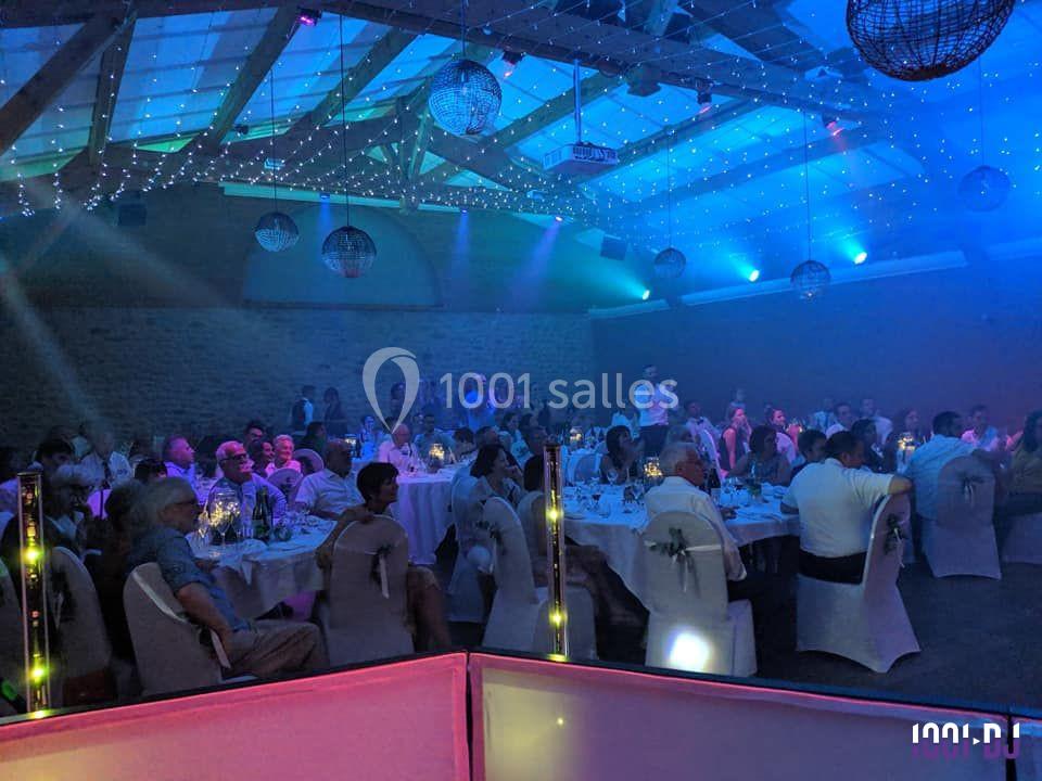 Salle de réception illuminée avec des invités assis à des tables rondes, sous un éclairage coloré et des décorations…