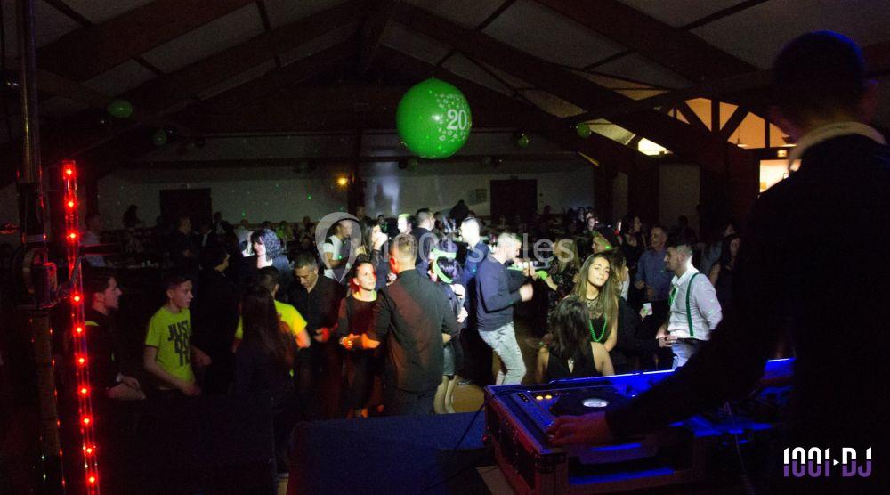 Des personnes dansent et socialisent dans une salle sombre éclairée par des lumières colorées, avec un DJ au premier plan.