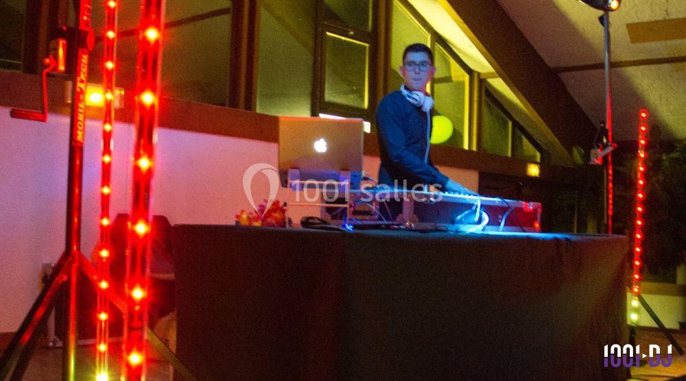 Un DJ mixant sur une table équipée d'un ordinateur portable, entouré de lumières colorées dans une salle.