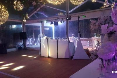 Salle de réception en plein air sous une verrière, avec tables décorées, nappes blanches et éclairage chaleureux.