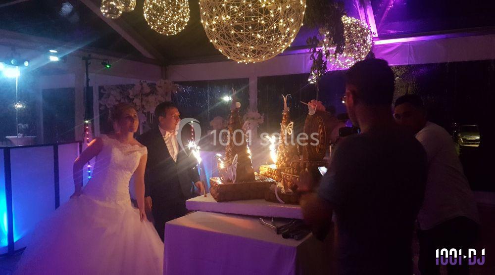 Un couple en tenue de mariage pose devant une table décorée avec des desserts et des étincelles sous des lumières suspendues.