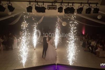 Salle de réception en plein air sous une verrière, avec tables décorées, nappes blanches et éclairage chaleureux.