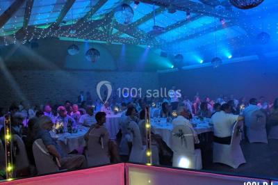 Salle de réception en plein air sous une verrière, avec tables décorées, nappes blanches et éclairage chaleureux.