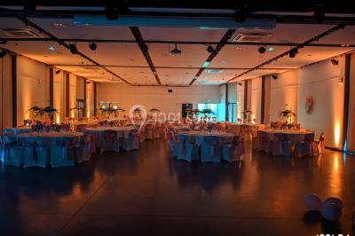 Salle de réception en plein air sous une verrière, avec tables décorées, nappes blanches et éclairage chaleureux.