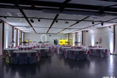 Salle de réception en plein air sous une verrière, avec tables décorées, nappes blanches et éclairage chaleureux.