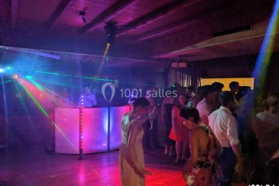 Salle de réception en plein air sous une verrière, avec tables décorées, nappes blanches et éclairage chaleureux.