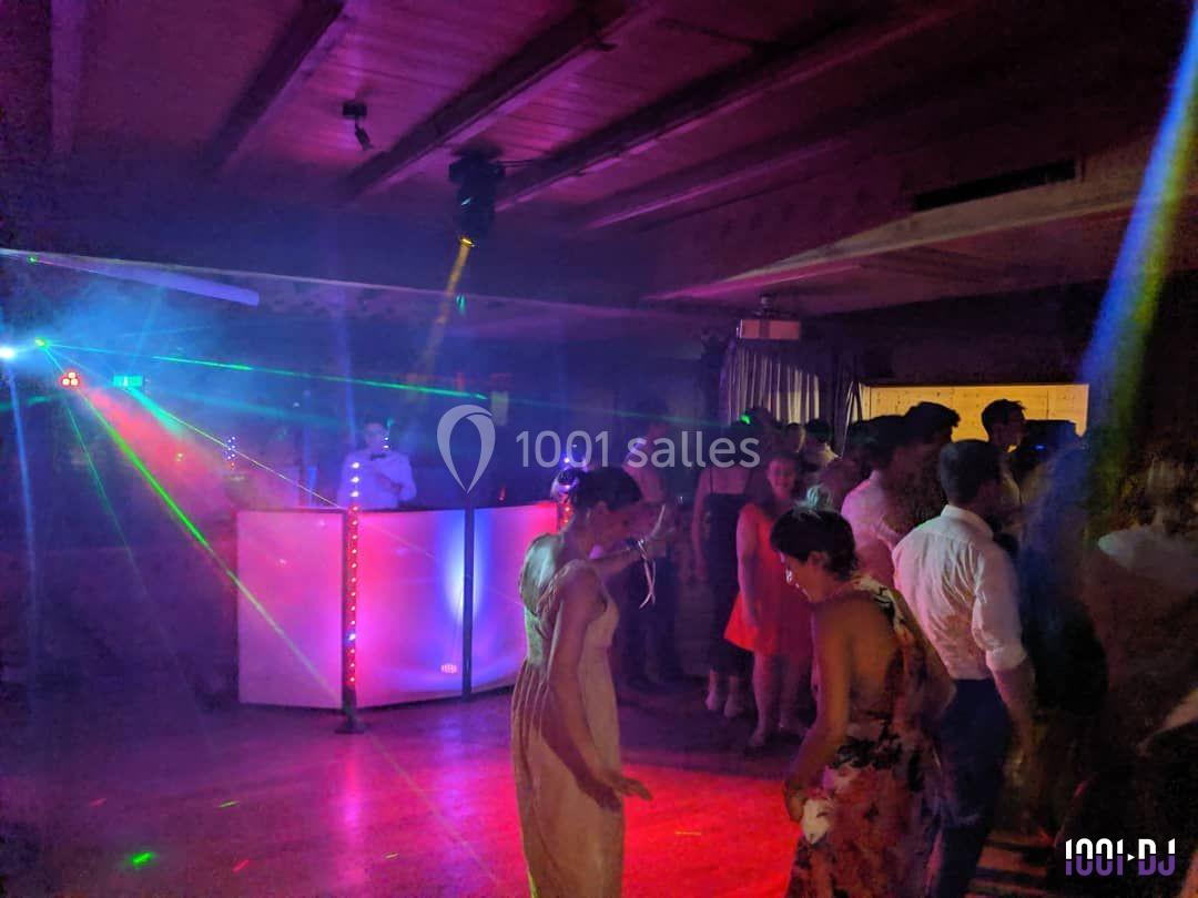 Des personnes dansent sur une piste éclairée par des lumières colorées, avec un DJ en arrière-plan.