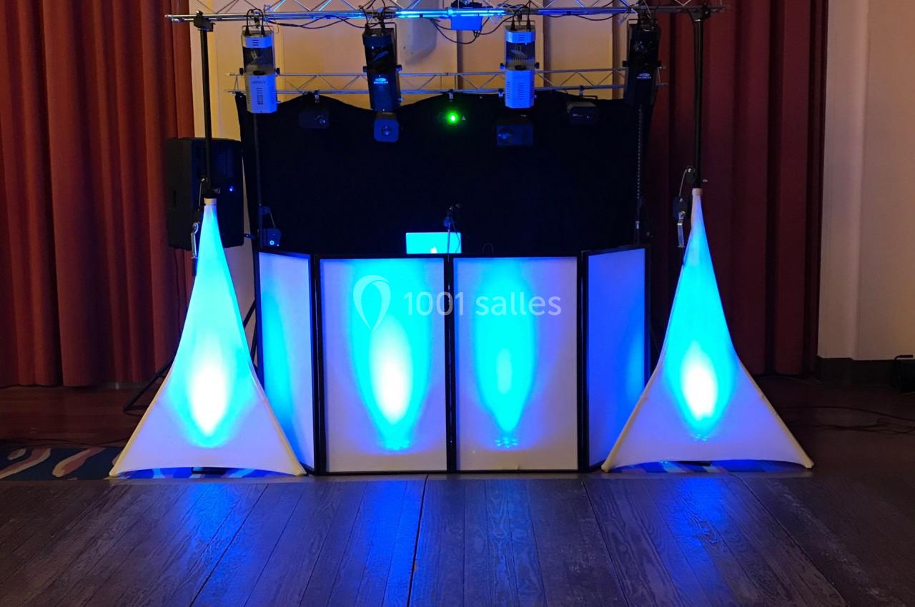 Équipement de sonorisation et éclairage avec lumières bleues installé dans une salle avec rideaux rouges.