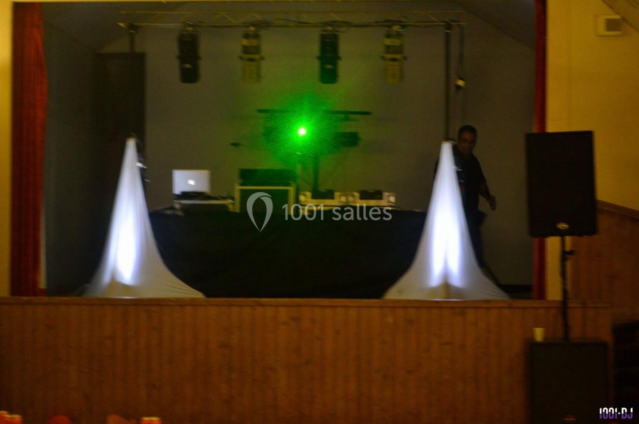 Scène de spectacle avec équipements audio et lumière, incluant un laser vert et un technicien en arrière-plan.