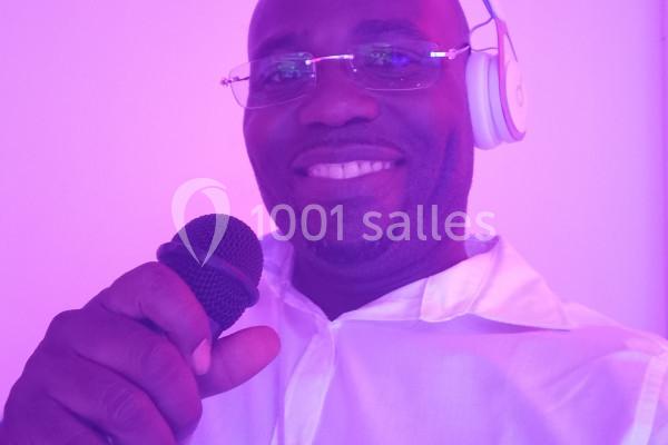 Homme souriant portant un casque audio et tenant un microphone dans un éclairage violet.