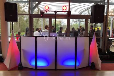 Console de DJ éclairée en bleu et rouge, installée dans une salle vitrée avec des invités en arrière-plan.