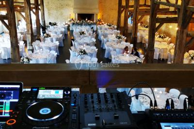 Console de DJ éclairée en bleu et rouge, installée dans une salle vitrée avec des invités en arrière-plan.