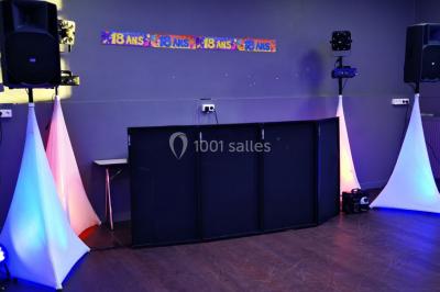 Console de DJ éclairée en bleu et rouge, installée dans une salle vitrée avec des invités en arrière-plan.