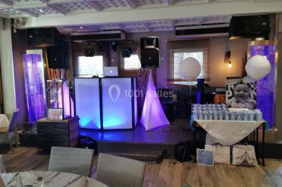 Console de DJ éclairée en bleu et rouge, installée dans une salle vitrée avec des invités en arrière-plan.