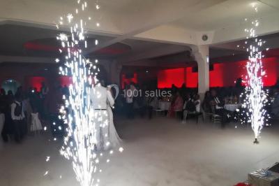 Console de DJ éclairée en bleu et rouge, installée dans une salle vitrée avec des invités en arrière-plan.