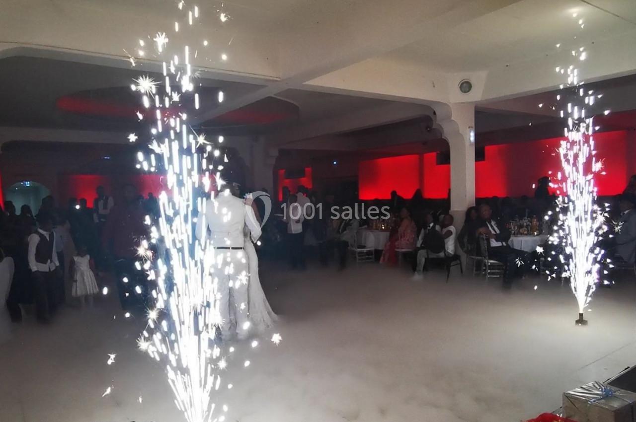 Salle de réception avec des invités assis, éclairages rouges et jets d'étincelles au premier plan.