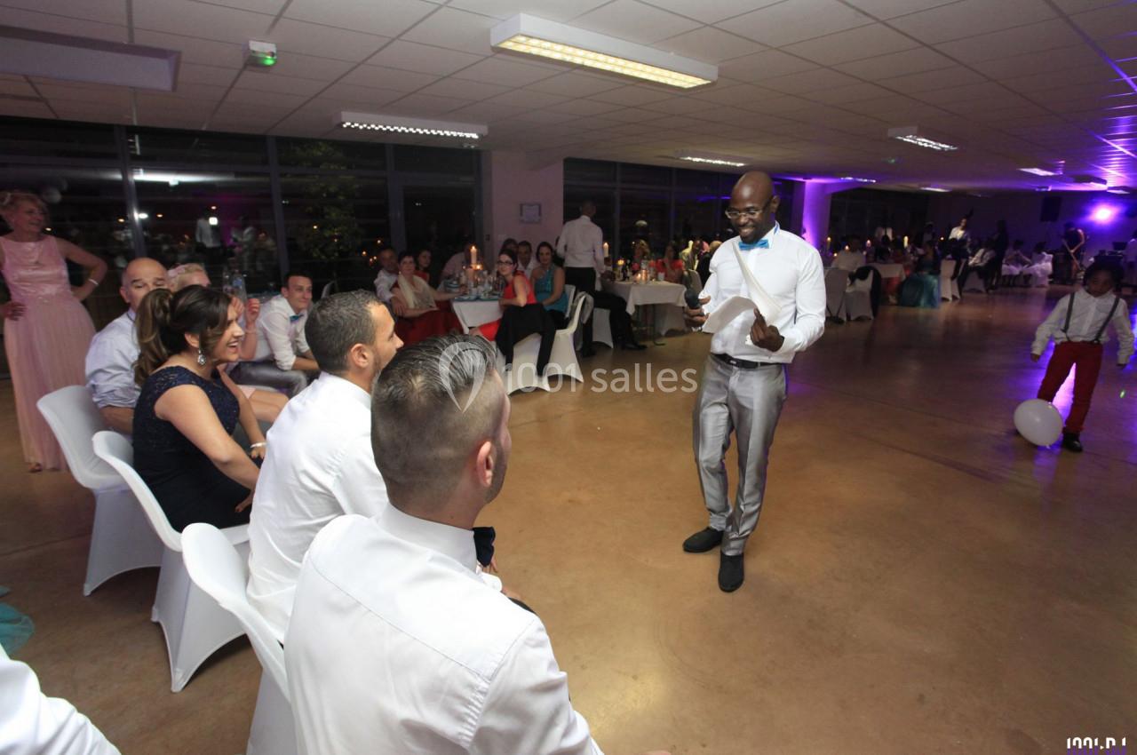 Un homme debout en costume parle à des invités assis lors d'une réception dans une salle éclairée.