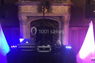 Console de DJ éclairée en bleu et rouge, installée dans une salle vitrée avec des invités en arrière-plan.