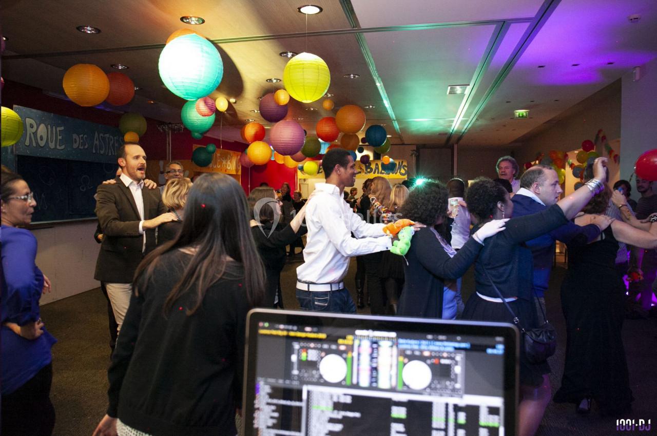 Des personnes dansent dans une salle décorée de lanternes colorées, avec une table de mixage au premier plan.
