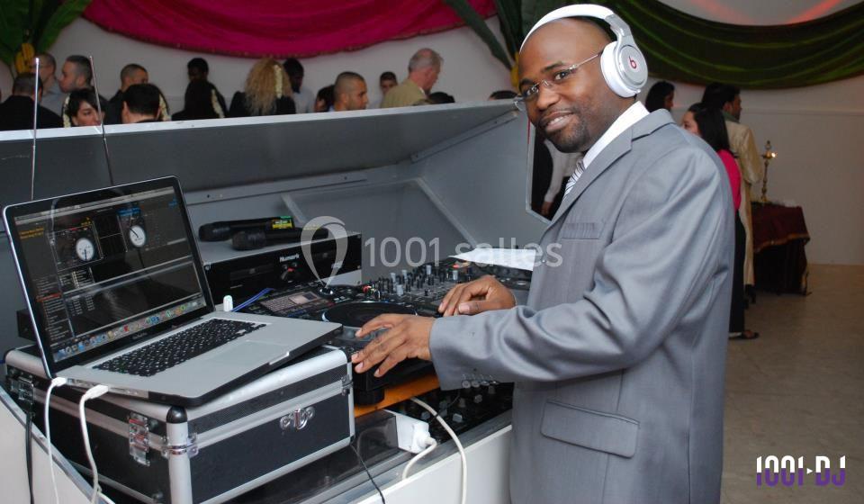 Un DJ en costume mixe de la musique avec un ordinateur portable et une table de mixage lors d'un événement.