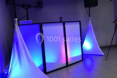 Console de DJ éclairée en bleu et rouge, installée dans une salle vitrée avec des invités en arrière-plan.