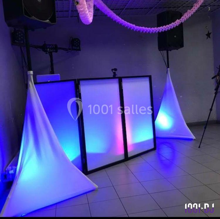 Console de DJ éclairée par des lumières colorées, entourée de haut-parleurs et de décorations suspendues.