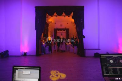 Console de DJ éclairée en bleu et rouge, installée dans une salle vitrée avec des invités en arrière-plan.