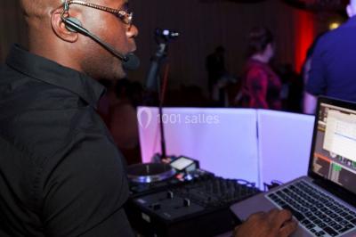 Console de DJ éclairée en bleu et rouge, installée dans une salle vitrée avec des invités en arrière-plan.