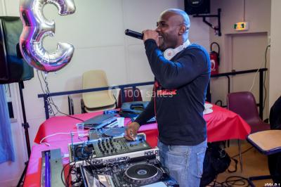 Console de DJ éclairée en bleu et rouge, installée dans une salle vitrée avec des invités en arrière-plan.