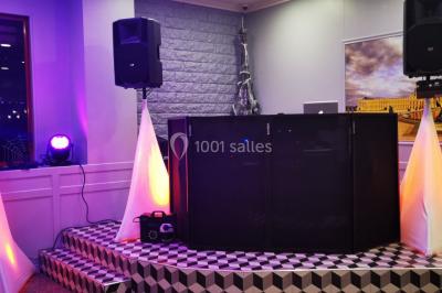 Console de DJ éclairée en bleu et rouge, installée dans une salle vitrée avec des invités en arrière-plan.