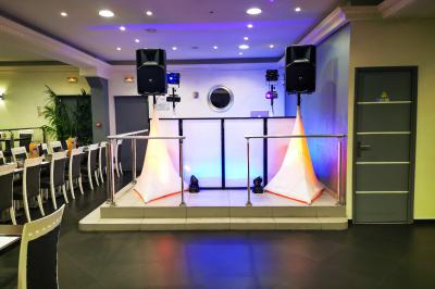 Console de DJ éclairée en bleu et rouge, installée dans une salle vitrée avec des invités en arrière-plan.