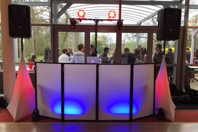 Console de DJ éclairée en bleu et rouge, installée dans une salle vitrée avec des invités en arrière-plan.