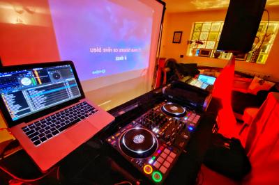 Console de DJ éclairée en bleu et rouge, installée dans une salle vitrée avec des invités en arrière-plan.