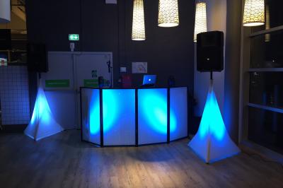 Console de DJ éclairée en bleu et rouge, installée dans une salle vitrée avec des invités en arrière-plan.