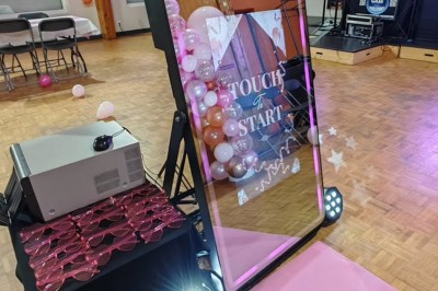 Console de DJ éclairée en bleu et rouge, installée dans une salle vitrée avec des invités en arrière-plan.