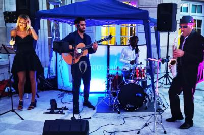 Salle de réception éclairée avec des lumières colorées, vue depuis une table de DJ équipée d'un ordinateur et de platines.