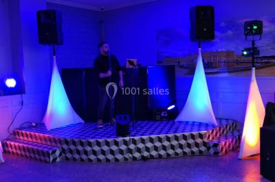 Salle de réception éclairée avec des lumières colorées, vue depuis une table de DJ équipée d'un ordinateur et de platines.